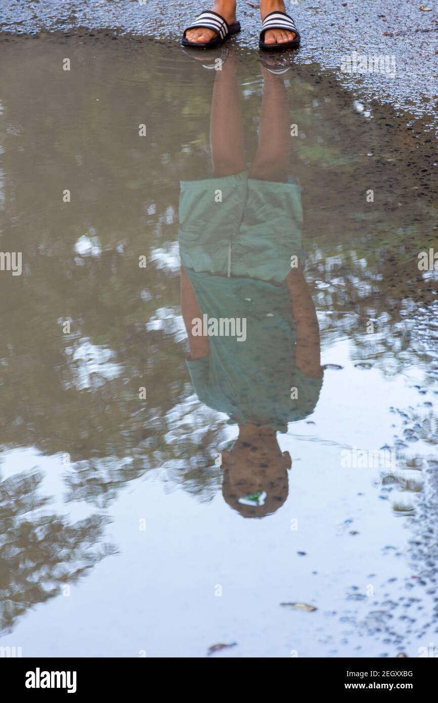 Riflessione di un ragazzo in un pozze d'acqua sulla strada Foto Stock