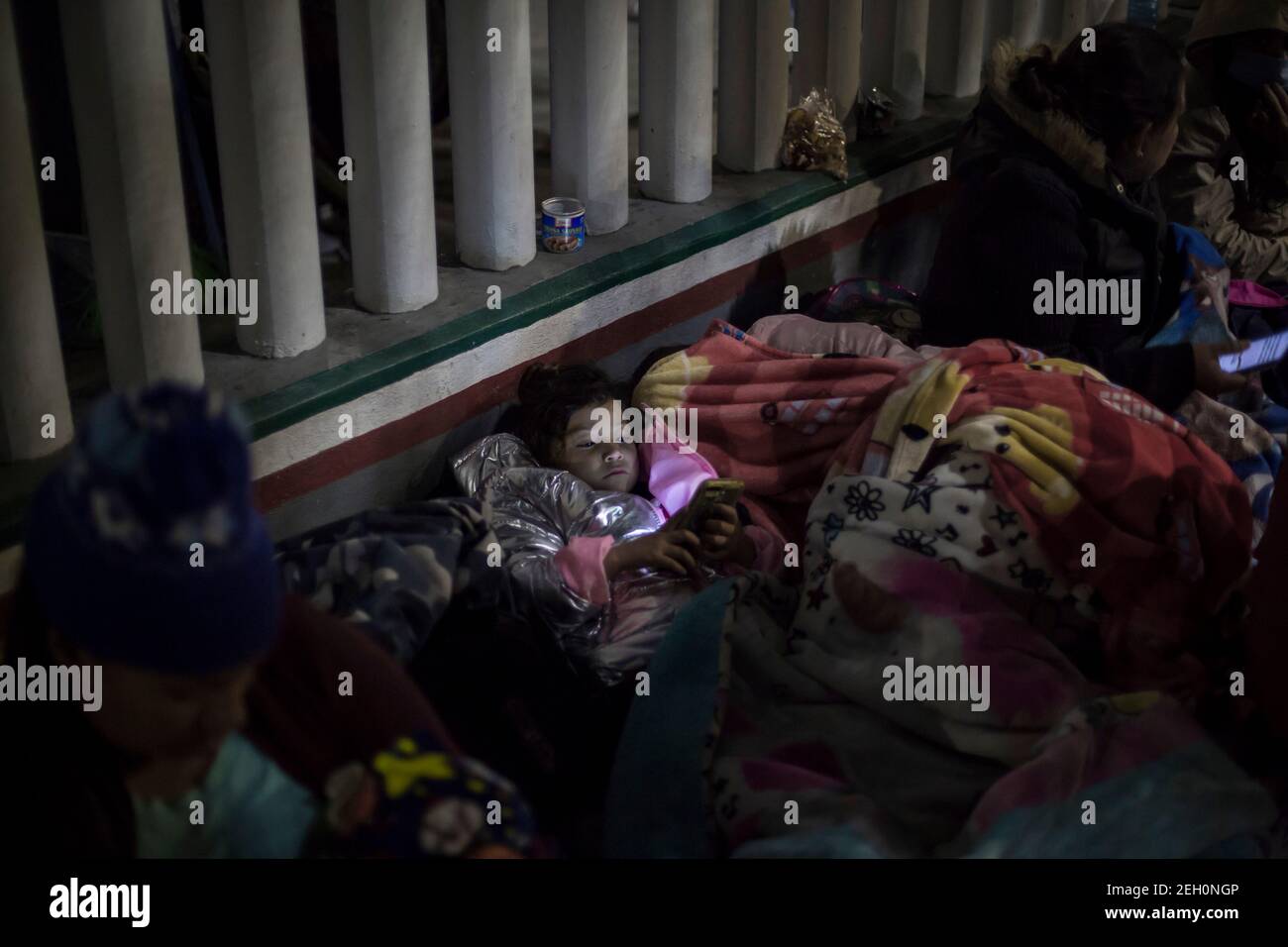 Tijuana, Messico. 19 Feb 2021. Una ragazza guarda un telefono cellulare mentre decine di migranti dormono accanto al National Migration Institute vicino al confine di El Chaparral. Dopo aver cambiato direzione sulla politica migratoria, il governo degli Stati Uniti sta ancora una volta consentendo ai richiedenti asilo di attraversare il confine. A partire da venerdì, i primi candidati arriveranno negli Stati Uniti per le audizioni dei tribunali e potranno rimanere nel paese per tutta la durata del loro procedimento. Credit: dpa Picture Alliance/Alamy Live News Foto Stock