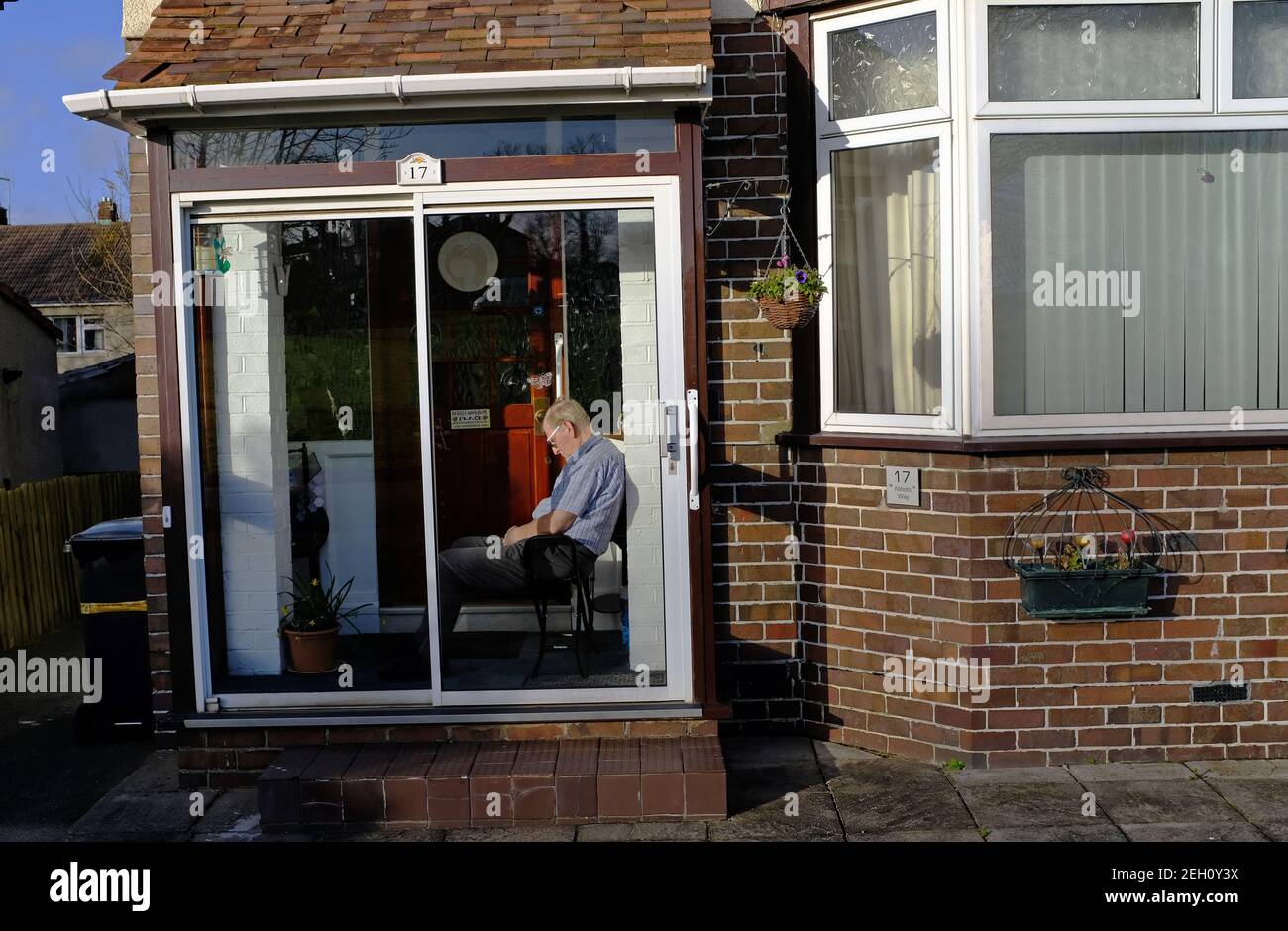 Un uomo addormentato nel suo portico anteriore a fine inverno durante il blocco. Foto Stock
