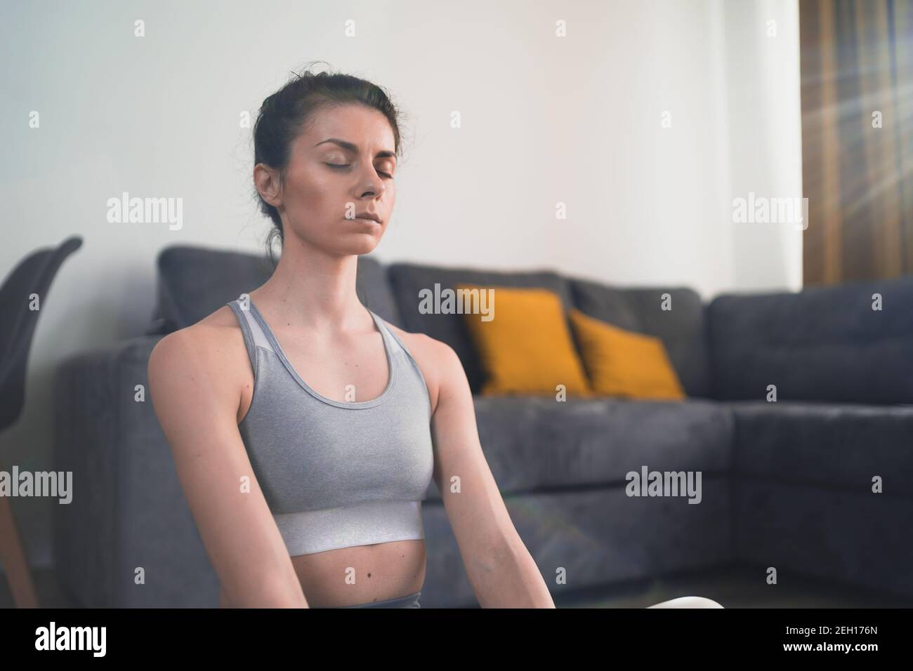 Sguardo ravvicinato di donna meditante in grigio sportivo seduta sopra pavimento a casa Foto Stock