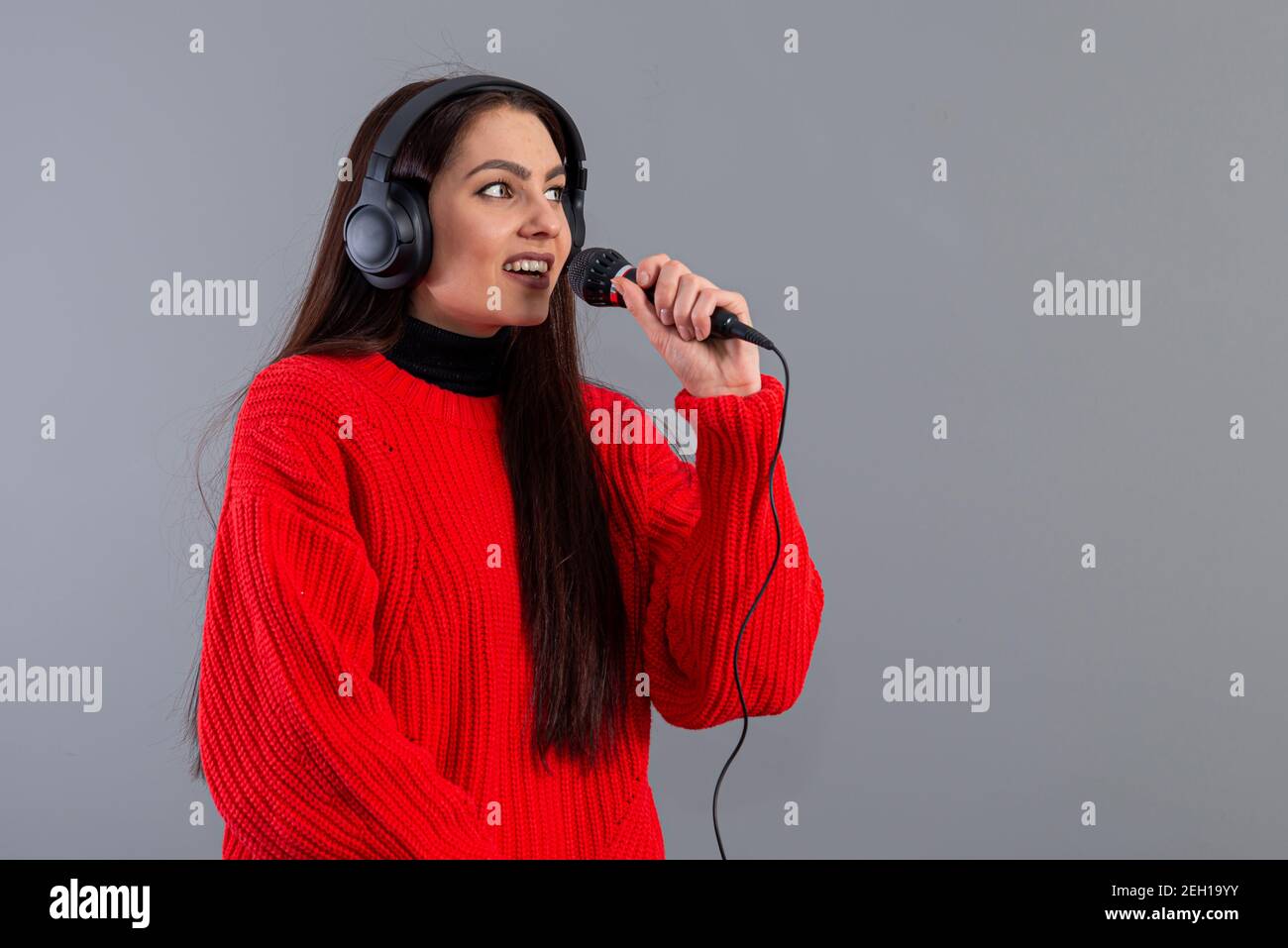 giovane ed emozionale bruna con cuffie e microfono vestito con un maglione  rosso canta karaoke, isolato su grigio Foto stock - Alamy
