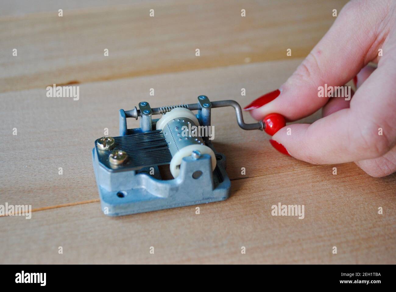 Closeup mano femminile che tiene una scatola di musica meccanica vintage con manico rosso su tavola di legno. Posizionare la scatola musicale su una superficie di legno per ottenere il massimo suono Foto Stock