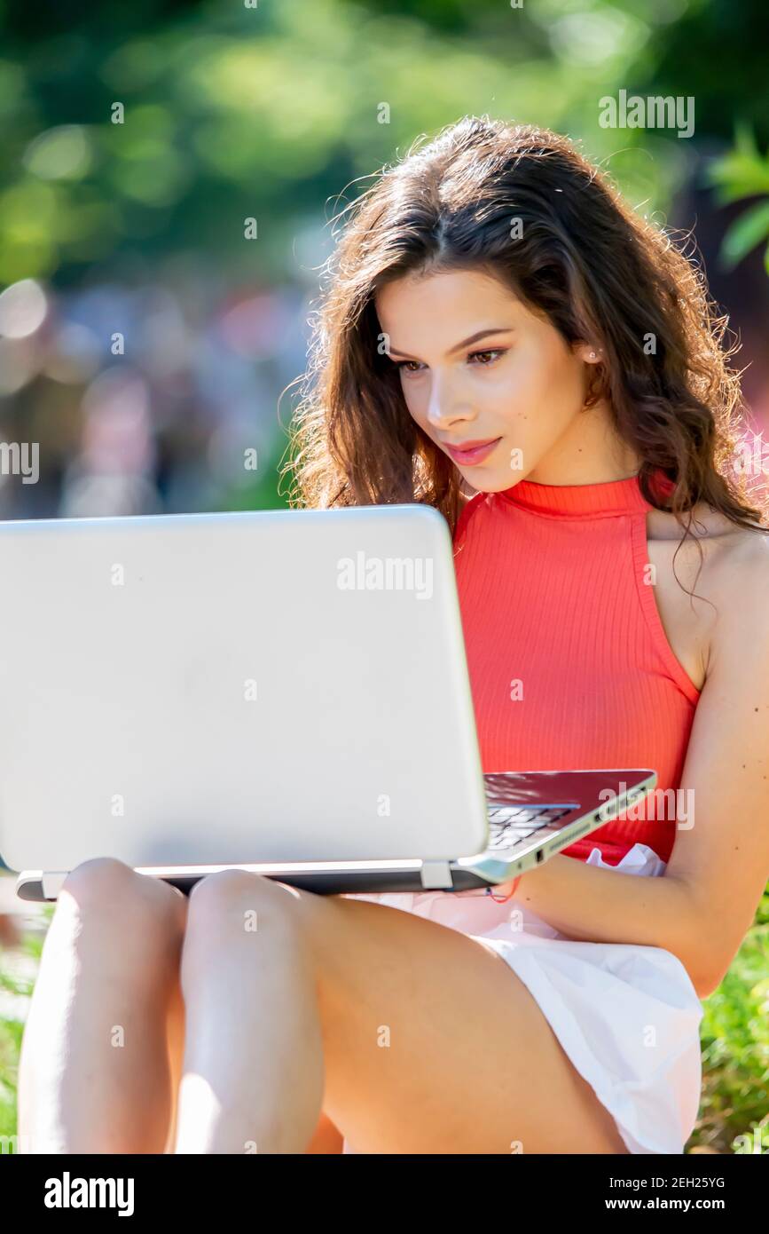 Giovane donna che usa un computer portatile all'aperto in un'estate intensa giorno Foto Stock