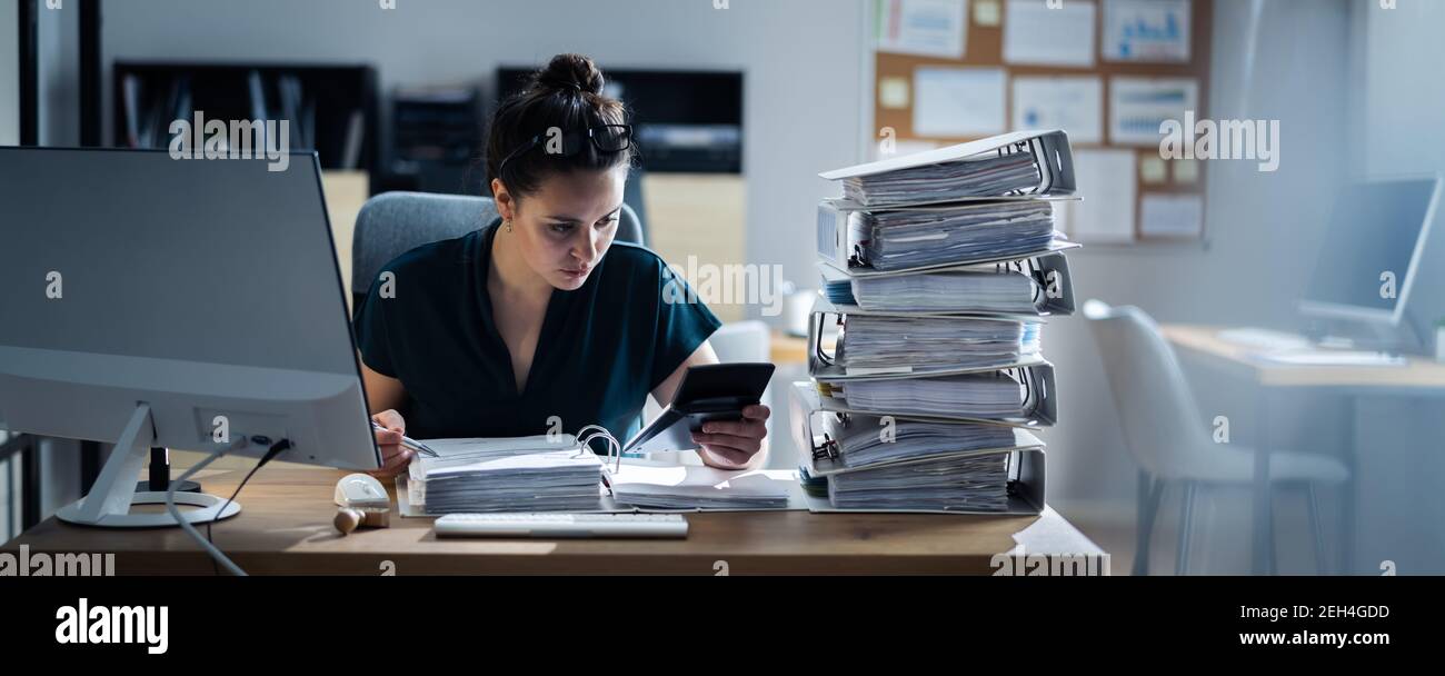 Giovane donna d'affari che lavora in ufficio con pila di cartelle sulla scrivania Foto Stock