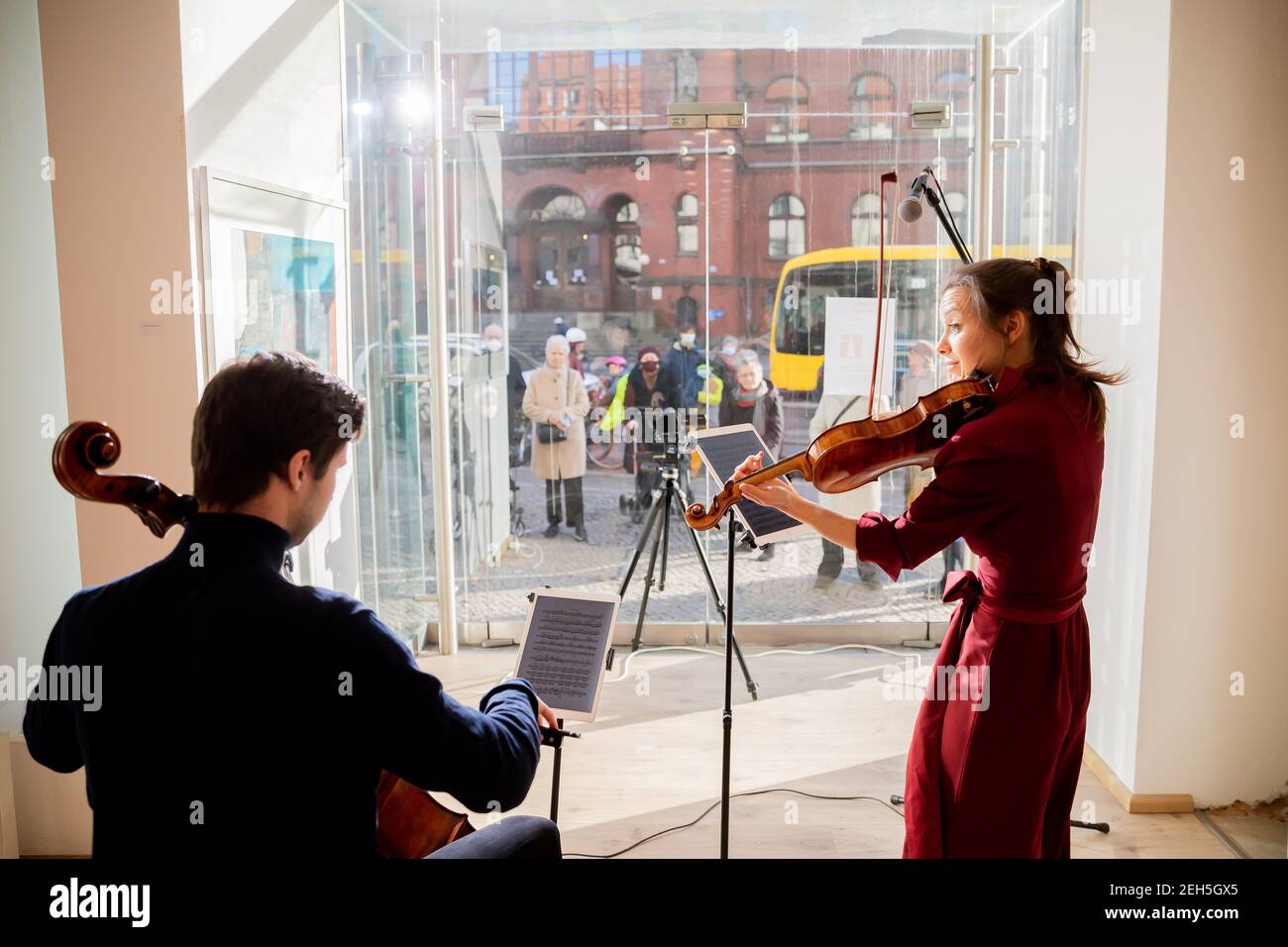 19 febbraio 2021, Berlino: Johanna Staemmler, violinista e iniziatore dei cosiddetti 'Concerti della finestra', si esibisce con suo marito Peter-Philipp Staemmler, violista, nella vetrina di una galleria di Berlino-Pankow di fronte ad un pubblico in piedi per strada. La musica viene trasmessa all'esterno tramite un sistema audio. Molti di questi spettacoli sono previsti come parte della serie 'Concerti finestra'. Foto: Christoph Soeder/dpa Foto Stock