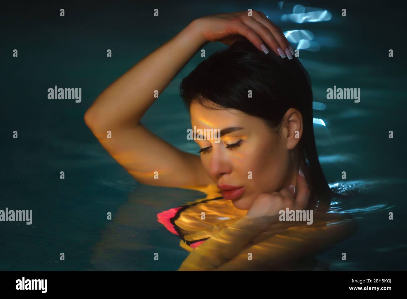 Ritratto notturno di donna brunette che nuotano in piscina con acqua minerale calda nella spa di balneoterapia. Il viso della bellezza è illuminato dalle luci notturne in piscina. Foto Stock