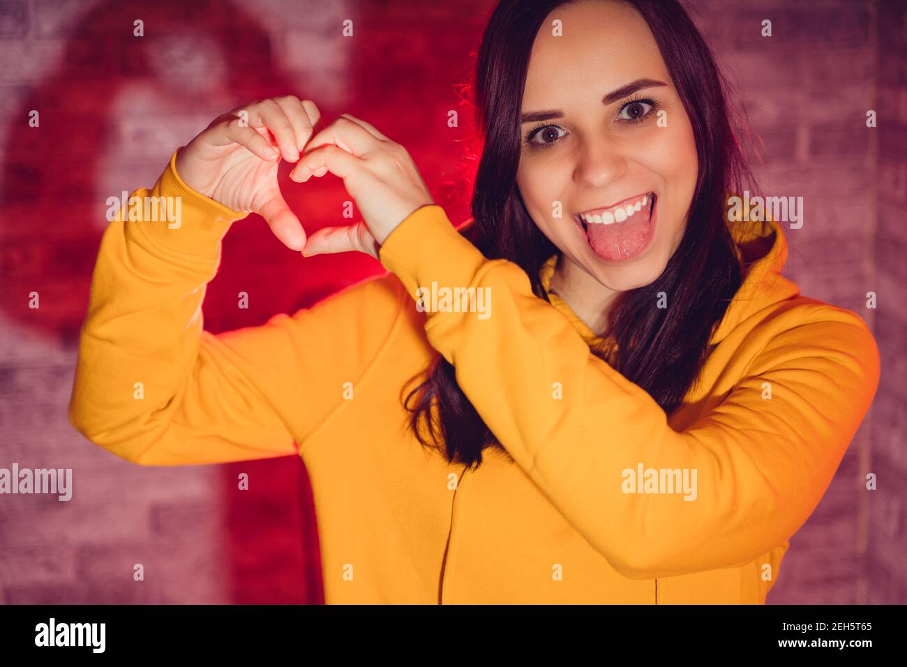 Ritratto di giovane donna che mostra il segno del cuore con le mani. Primo piano di Happy brunette mostra segno d'amore su sfondo retroilluminato Foto Stock