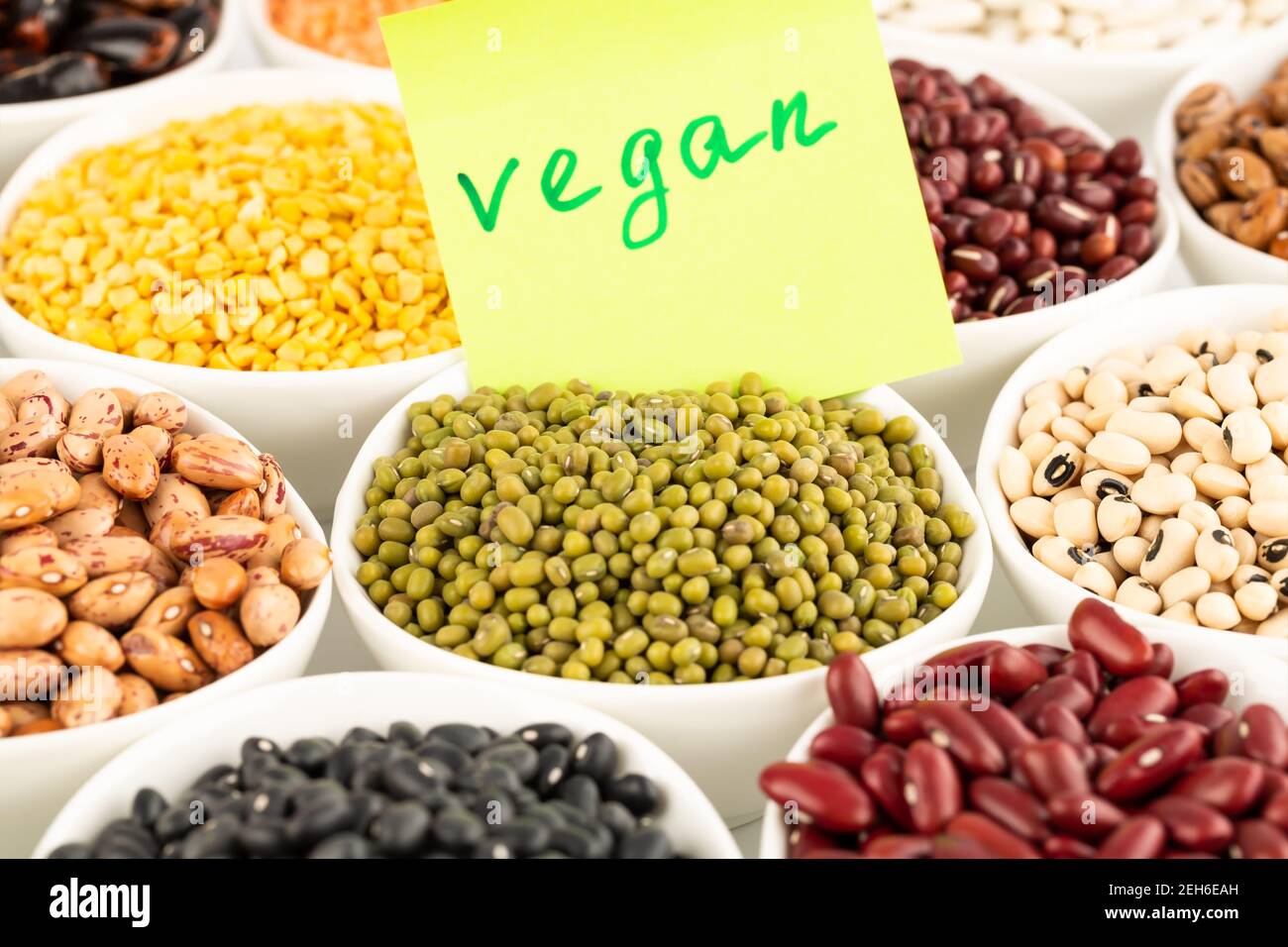 La raccolta di diversi fagioli e piselli nelle ciotole in ceramica con avviso vegano. Foto Stock