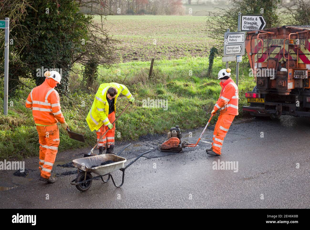 BUCKINGHAM, Regno Unito - 14 dicembre 2020. Lavori stradali, team di equipaggi stradali, uomini che indossano abiti arancioni ad alta visibilità. Riparare le buche in un paese rurale Foto Stock
