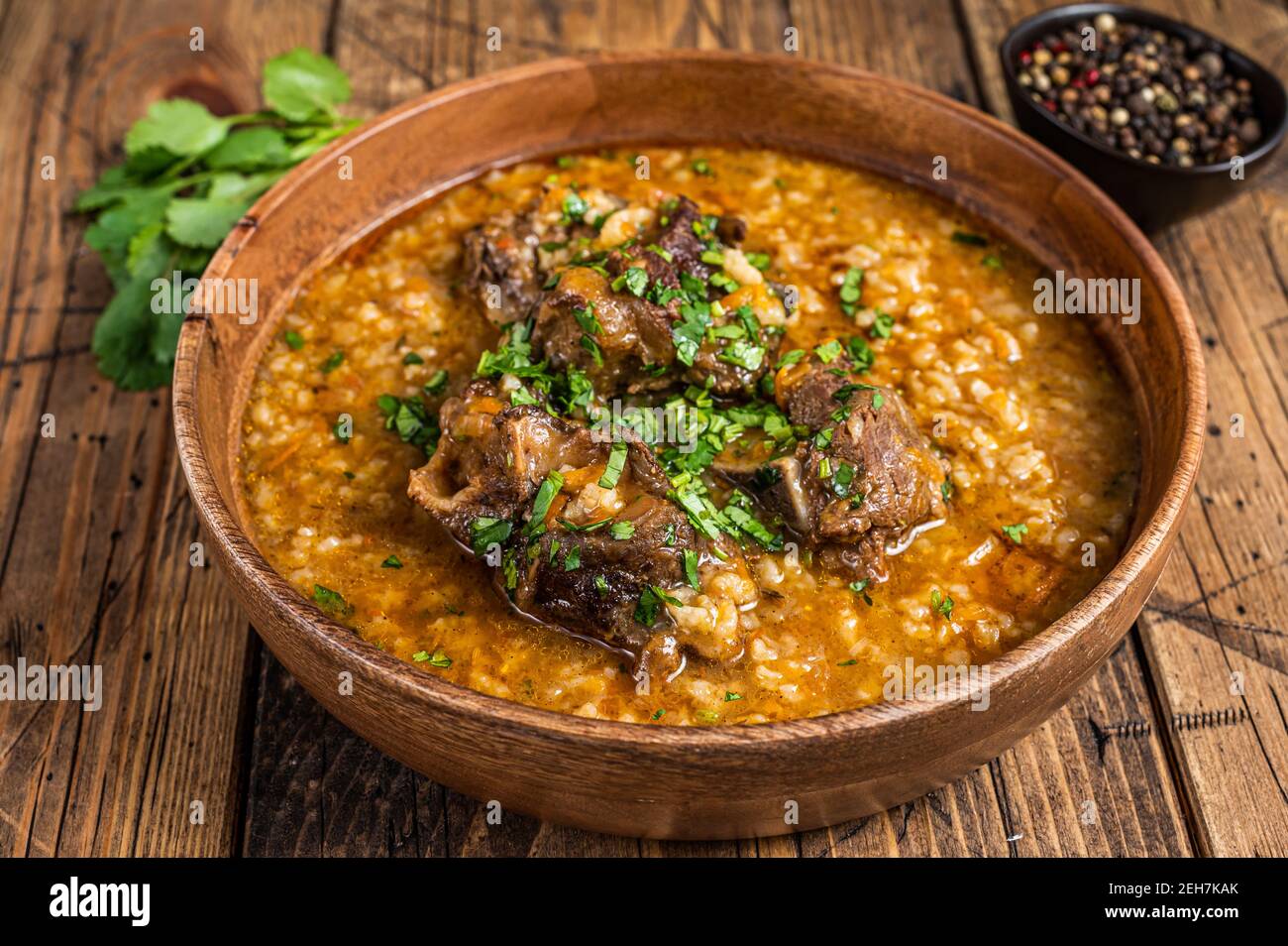 Zuppa georgiana di carne di agnello Kharcho con riso, pomodori e spezie in una ciotola di legno. Sfondo di legno. Vista dall'alto Foto Stock