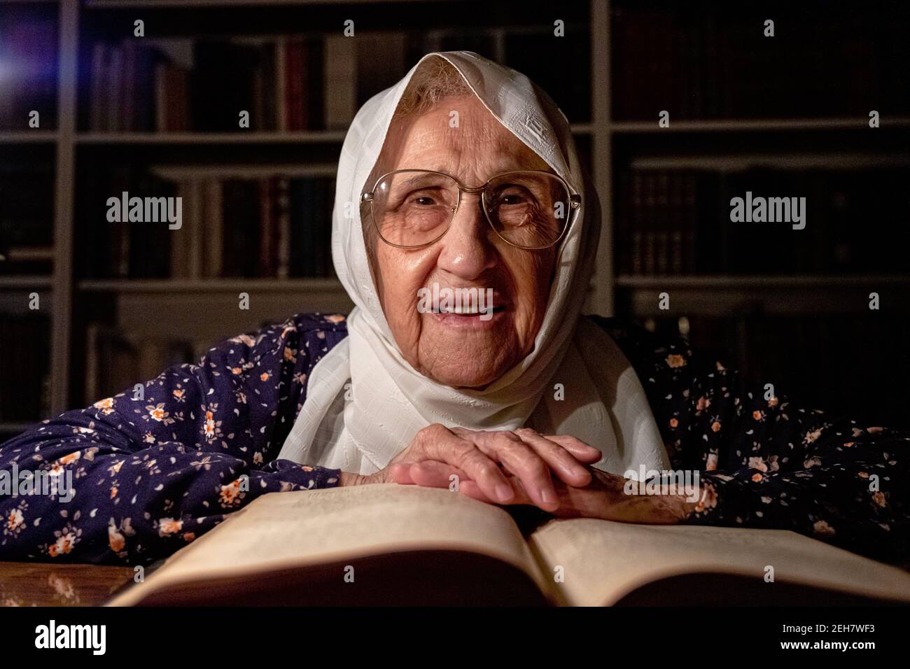 Donna anziana che legge libri in camera oscura con le candele di luce Foto Stock