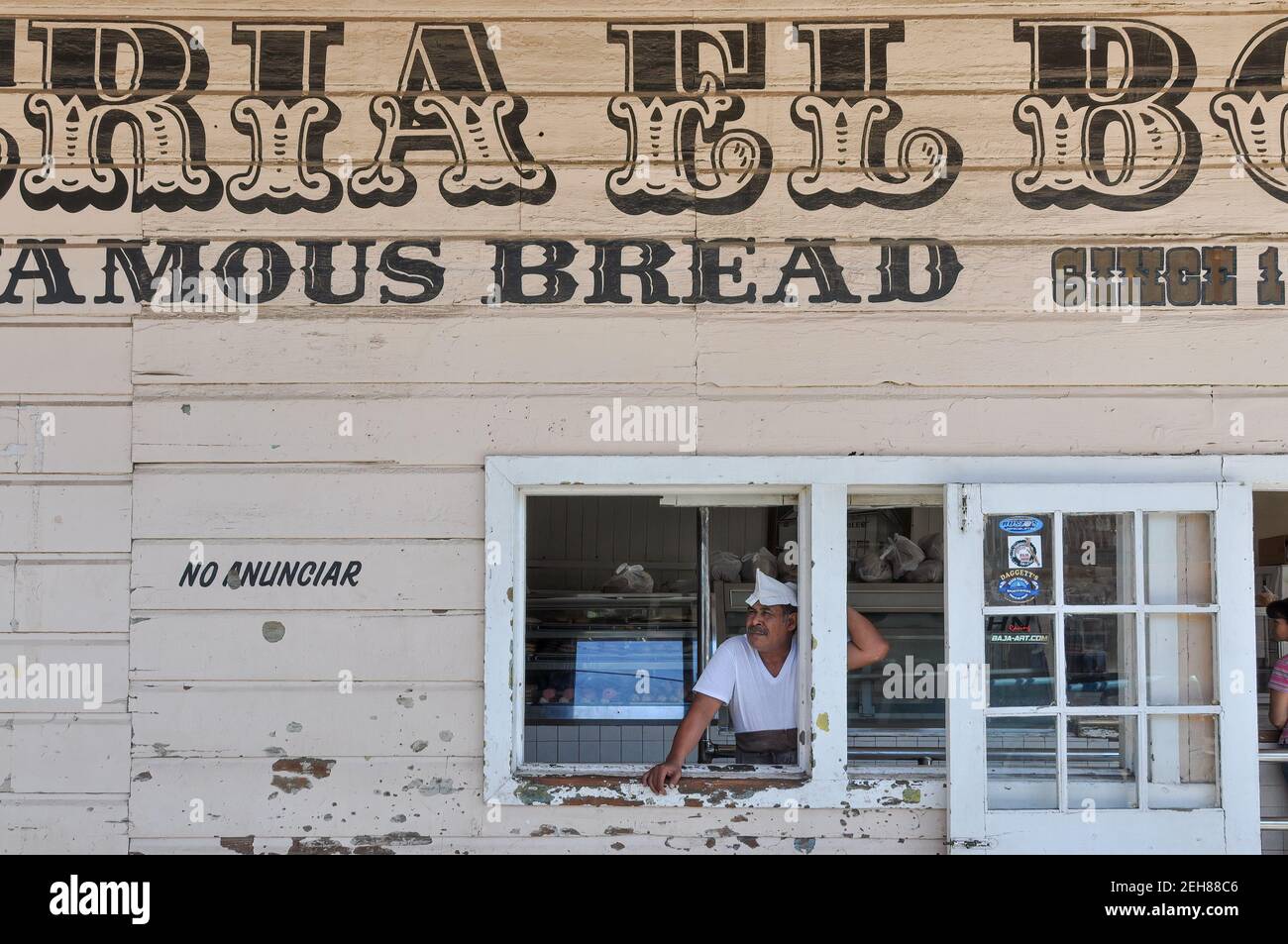 Un uomo in t-shirt bianca, grembiule e cappello da panettiere si staglia guardando fuori la finestra di El Boleo, una famosa panetteria a Santa Rosalia, Baja California, Messico. Foto Stock