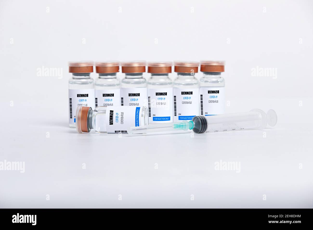 Flaconcini di vetro trasparente con vaccino COVID-19 test e siringa sulla superficie bianca. Foto Stock