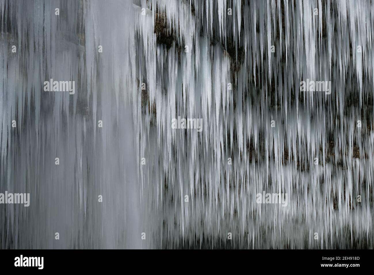 Belle lunghe cicette di una cascata ghiacciata. Acqua che scorre e si schiantano e ghiaccio che sgocciola in una calura fredda e scura grotta di montagna Foto Stock