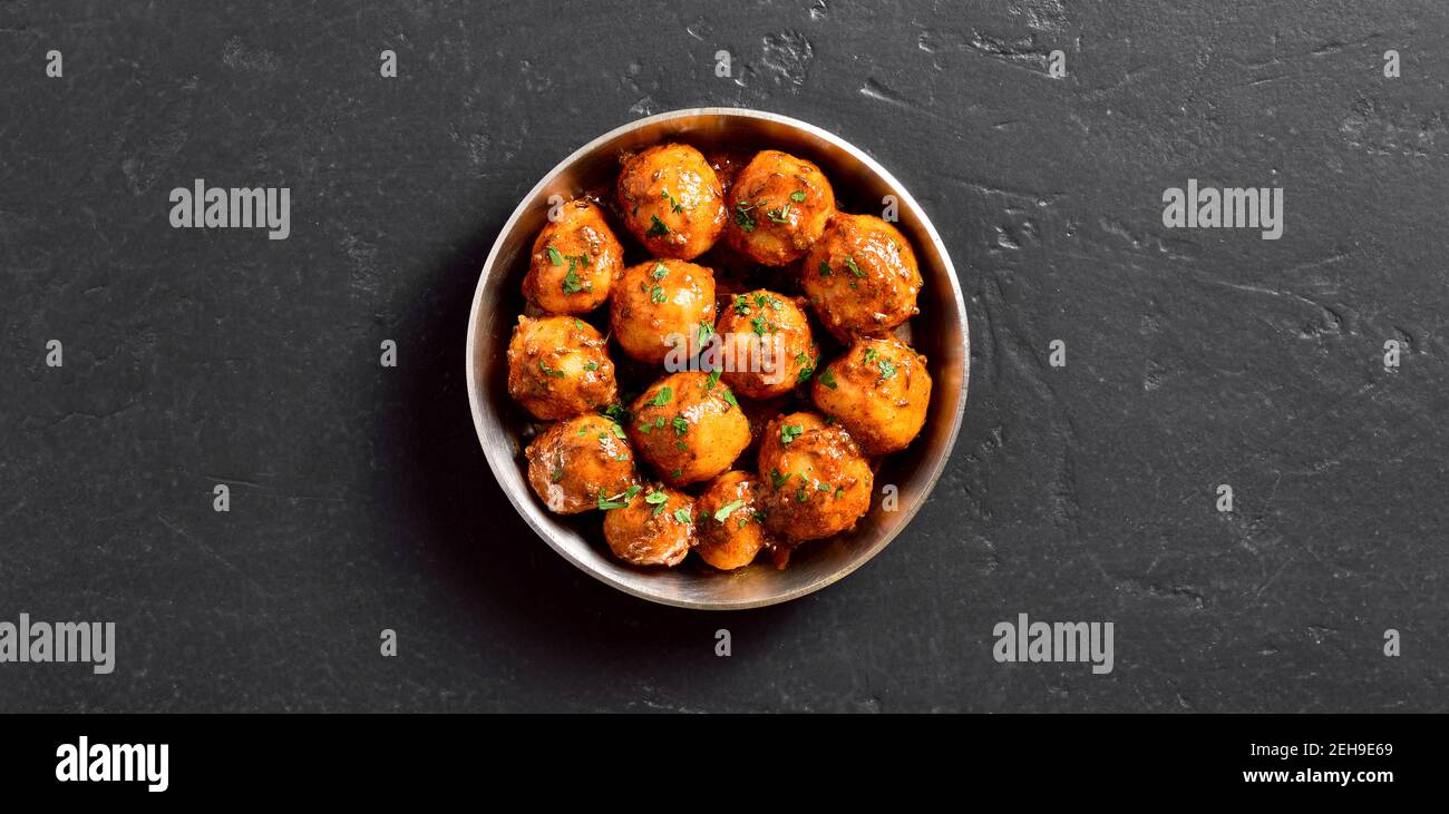 Patate Bombay. Pan patate fritte piccolo bambino con i semi di jeera e coriandolo in ciotola su sfondo di pietra scuro con spazio libero di testo. popolare indiano Foto Stock