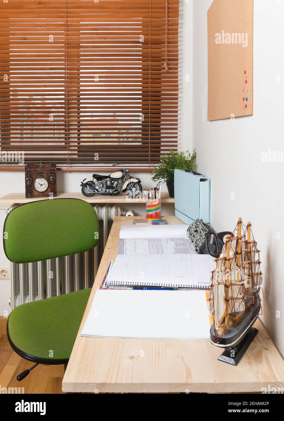 Piccola stanza studio a casa senza persone. Sedia verde accanto a una scrivania in legno con foglie e taccuini in cima in Spagna. Foto Stock