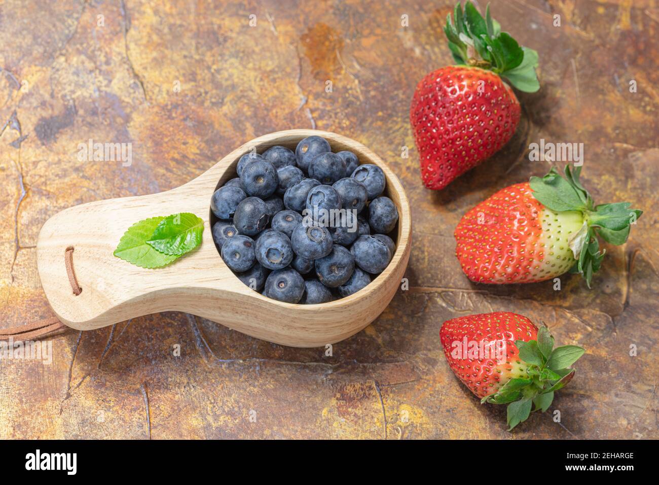 Mirtilli freschi e fragole in una tazza di legno. Concetto di vitamine naturali. Foto di alta qualità Foto Stock
