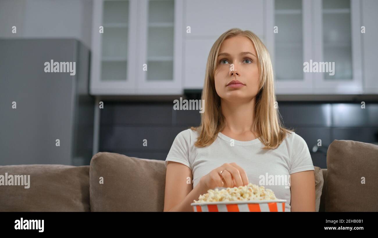 Vista frontale della bella donna con ammirazione guardando la TV e mangiando popcorn. Concetto di buon fine settimana con film interessante e snack gustosi. Foto Stock