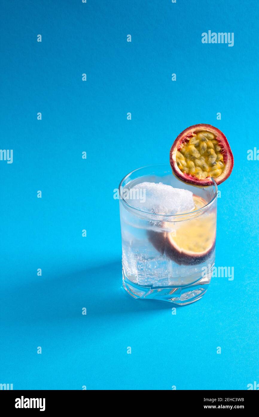 Un bicchiere d'acqua con una fetta di frutto della passione e cubetti di ghiaccio Foto Stock