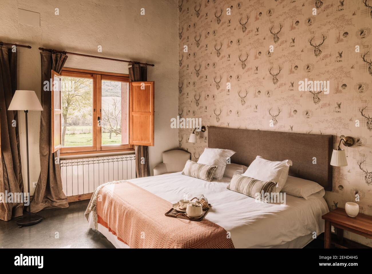 Interno di elegante camera da letto con comodo letto coperto di copriletto vicino alla finestra decorata con tende Foto Stock
