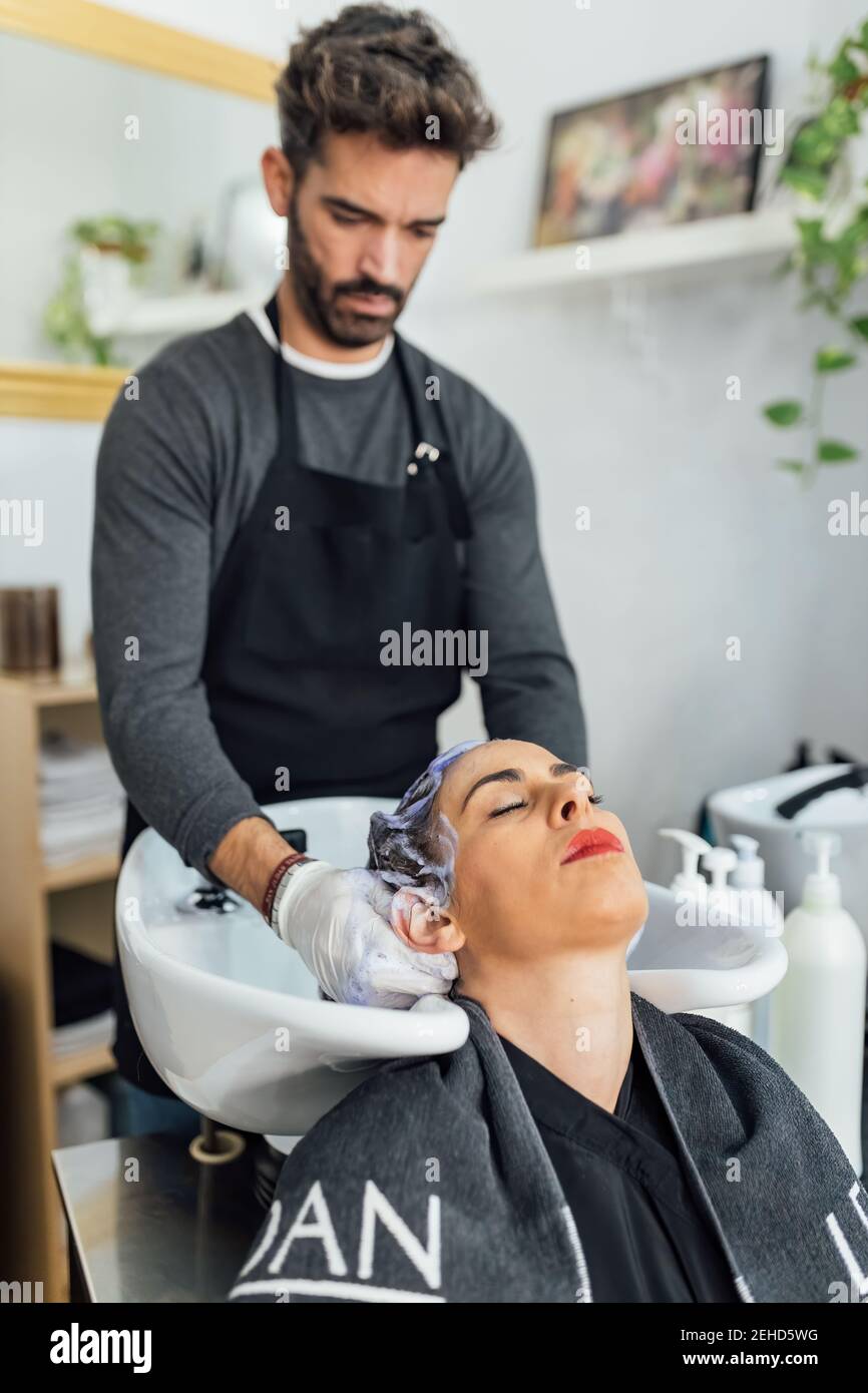 Serio giovane etnico maschile parrucchiere in grembiule lavaggio capelli di  cliente femminile in lavello dopo il taglio e la tintura in moderno salone  di bellezza Foto stock - Alamy