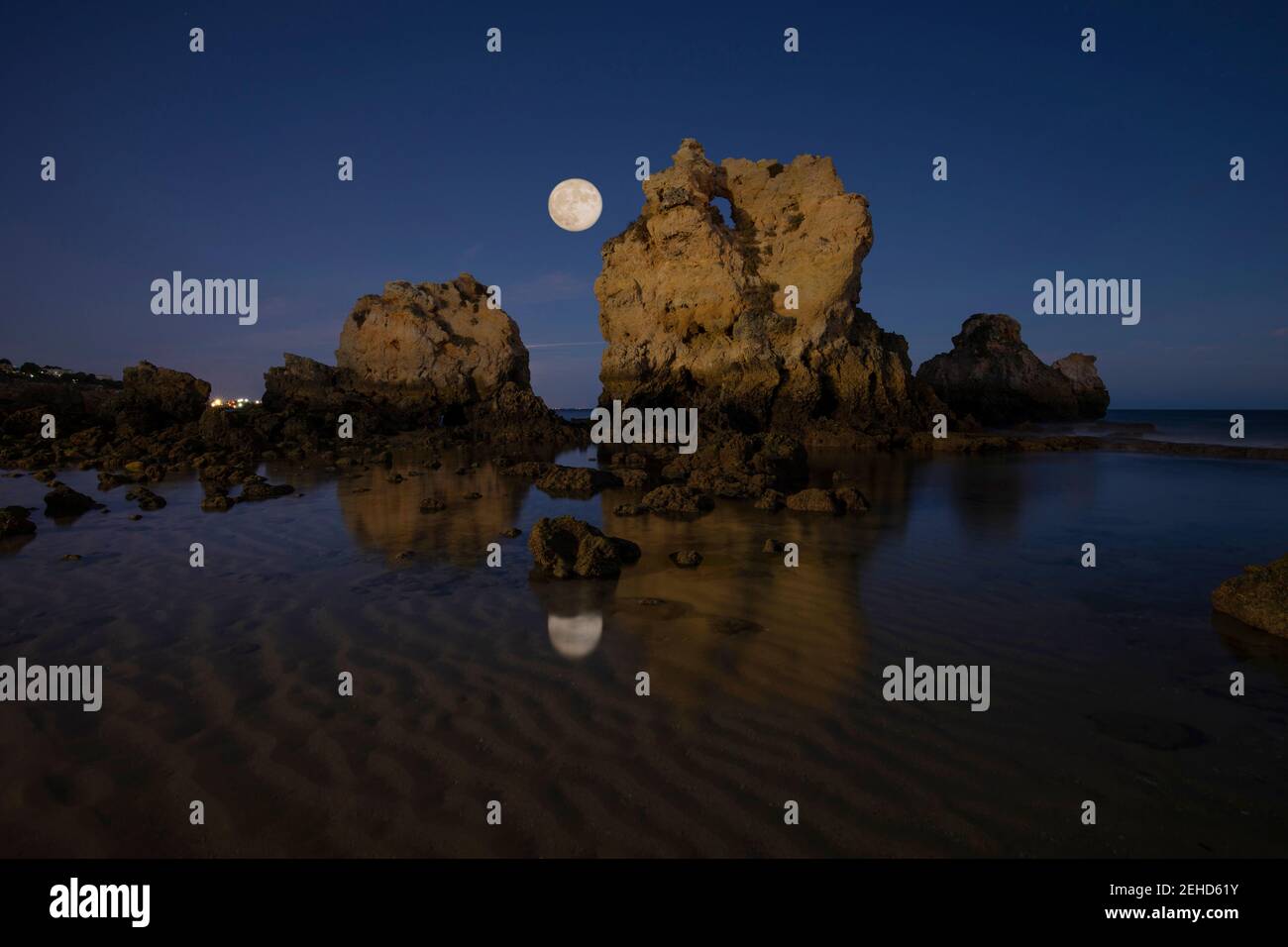 Vista panoramica della spiaggia di Arrifes con formazioni rocciose in puro mare increspato sotto cielo nuvoloso con luna di notte Algarve Portogallo Foto Stock