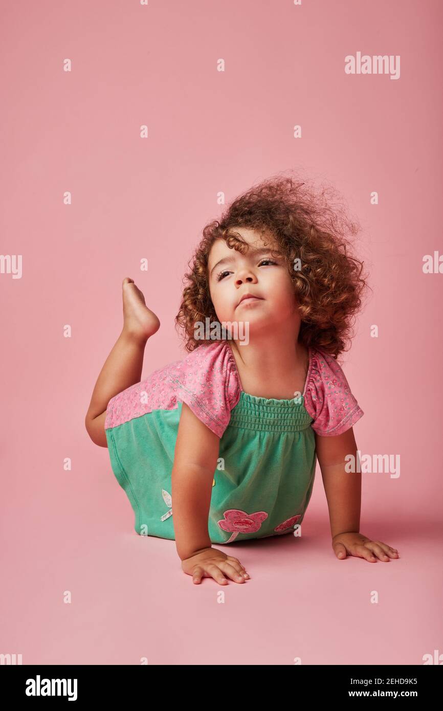 Adorabile bambino in abito con capelli ricci che guardano via appoggiandosi con le mani sul pavimento Foto Stock