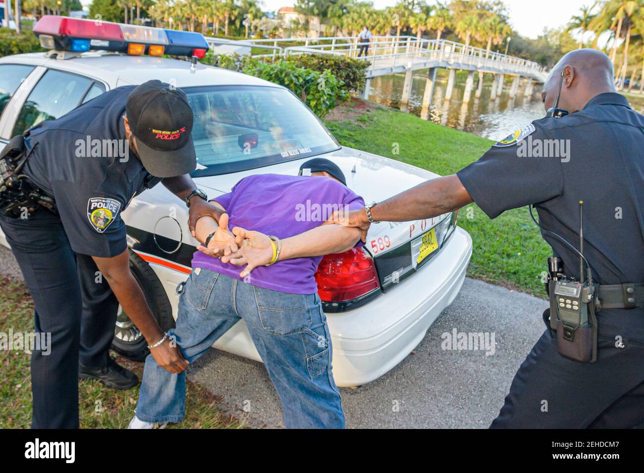 North Miami Beach Florida, Dipartimento di polizia, poliziotto nero poliziotti arresto uomo di arresto indossando manette che si frisking, mani dietro la schiena faccia in giù, Foto Stock