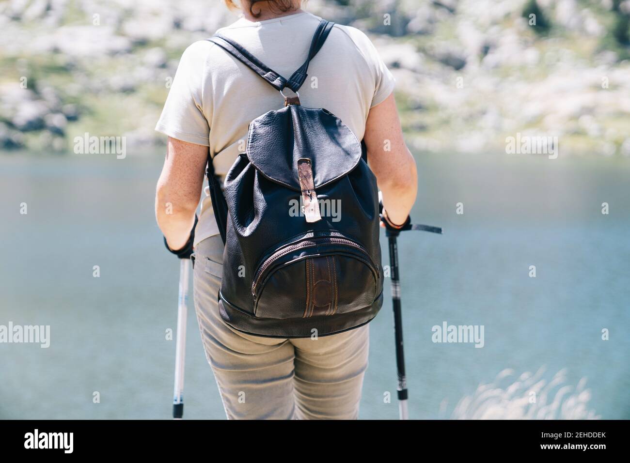 Vista posteriore anonimo escursionista femminile in piedi con bastoni da passeggio su La costa del fiume è sassosa nei Pirenei catalani, con il clima estivo soleggiato Foto Stock