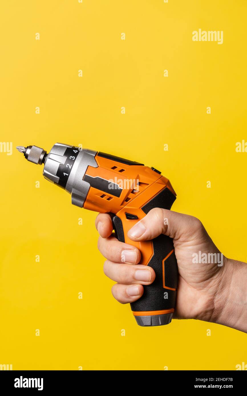 Mano di un uomo sconosciuto che tiene un cacciavite elettrico - presa maschio attrezzatura da lavoro su sfondo giallo brillante - ristrutturazione riparazione strumenti per apparecchiature elettriche Foto Stock