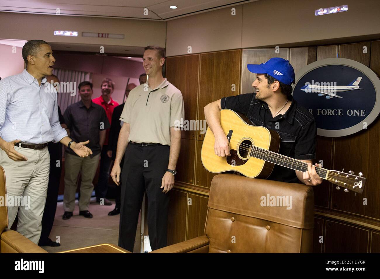 Il presidente Barack Obama conduce il canto di buon compleanno per Rob Nation, sovrintendente degli assistenti di volo presidenziali, mentre il cantante di paese Brad Paisley suona la chitarra su Air Force One al ritorno a casa dalle truppe in visita in Afghanistan, domenica 25 maggio 2014. Foto Stock