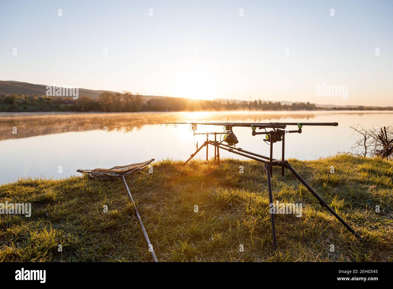 Le avventure di pesca, la pesca alla carpa. Il pescatore, al tramonto, è la pesca con carp fishing tecnica. Campeggio in riva al lago. Foto Stock