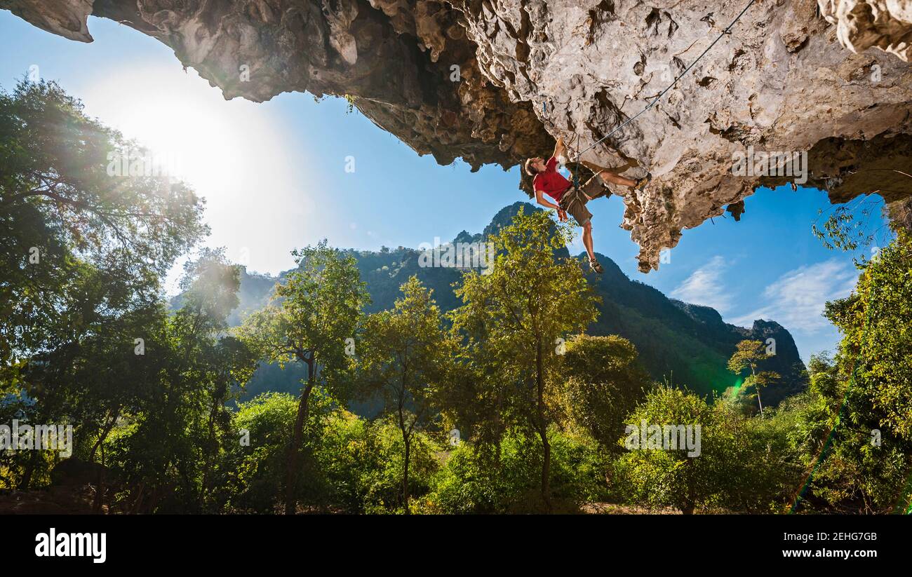 Uomo che sale su una scogliera di pietra calcarea a strapiombo in Laos Foto Stock