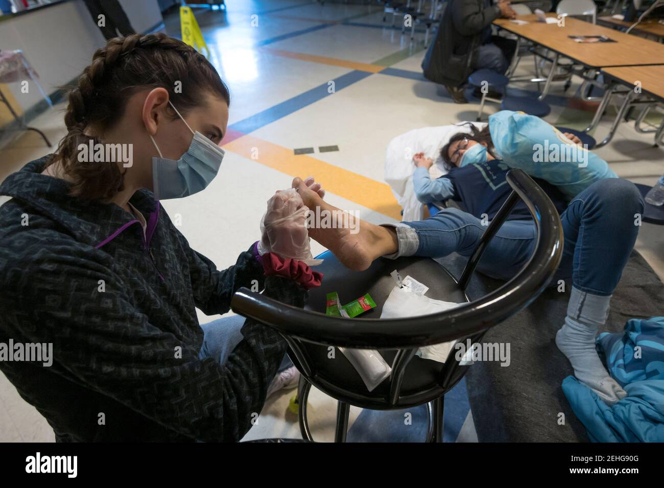 Austin, Texas USA, 19 febbraio 2021: Volontario Meagan Melhop (l), uno studente dell'Università del Texas, si prepara a pulire e bendare un possibile piede frostbitten di una donna senza casa che ripara per diversi giorni in una chiesa di Austin durante il tempo invernale severo. La donna ha detto che ha dormito fuori durante la prima notte del freddo devastante del Texas di questa settimana ma non ha coperto correttamente il suo piede. Credit: Bob Daemmrich/Alamy Live News Foto Stock