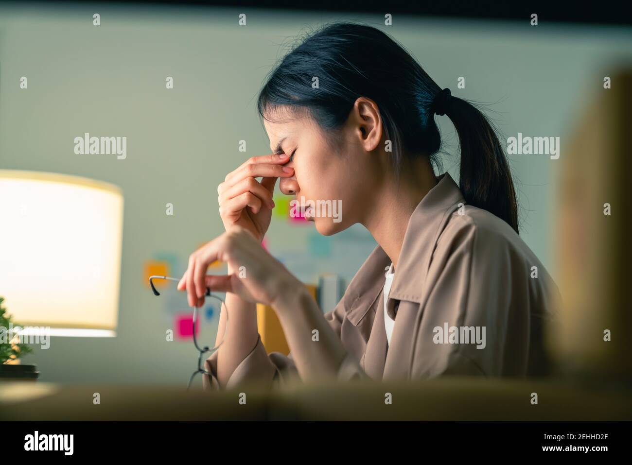 Giovane donna asiatica seduto e tenere bicchieri con le mani toccare le sopracciglia hanno un mal di testa perché l'emicrania. Foto Stock