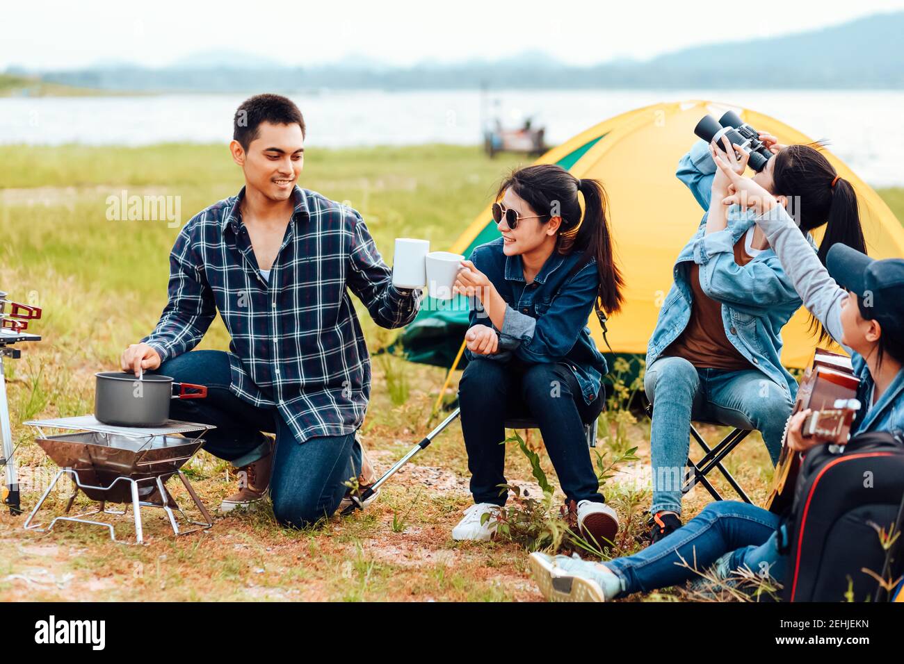 Un gruppo di amici si accampano felicemente vicino al lago per una vacanza. Una donna suona la chitarra per un amico da ascoltare. Foto Stock