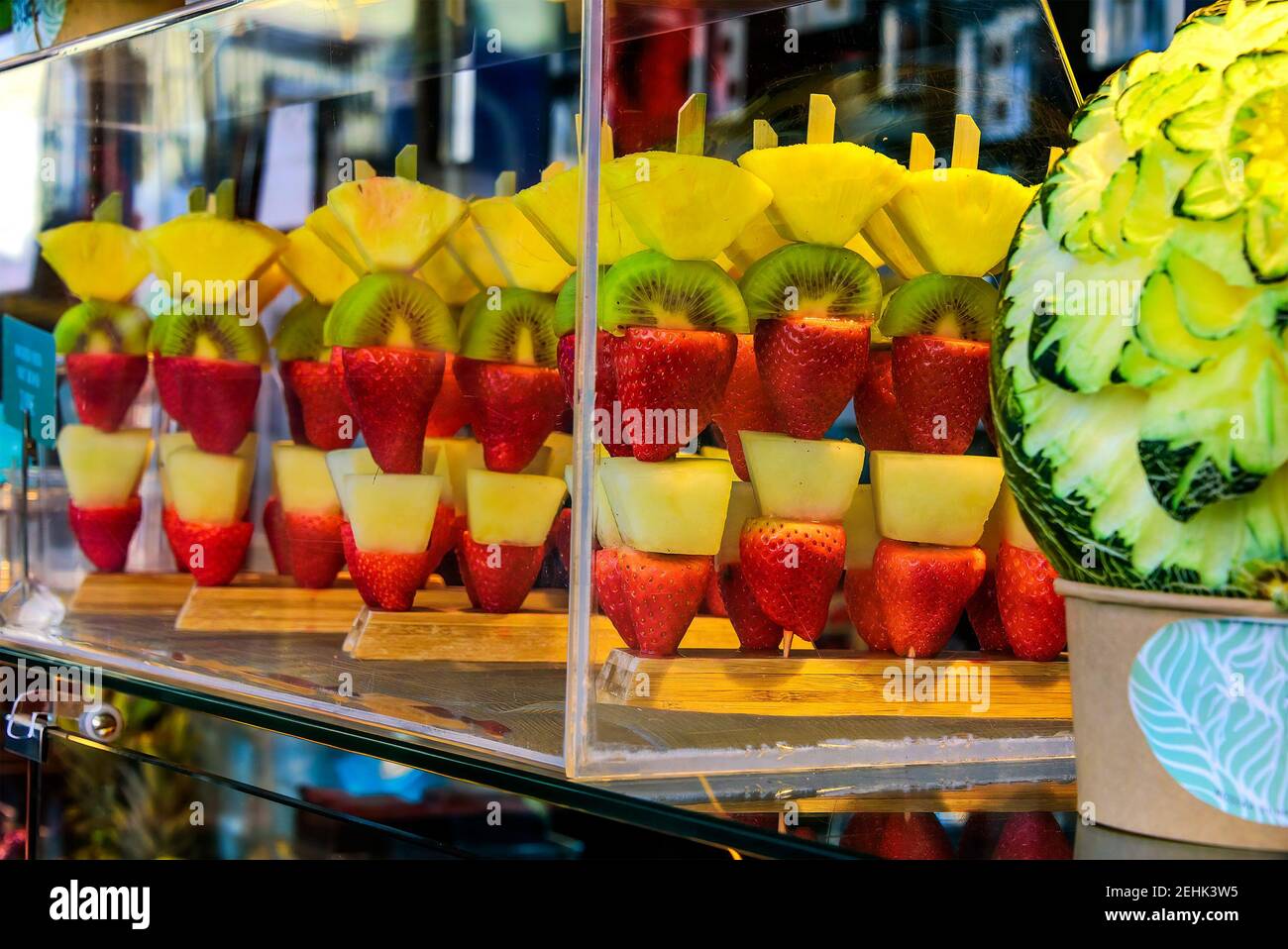 Pezzi di frutta esotica su bastoni, fragole, pere, kiwi e ananas. Visualizzazione precisa in una custodia in vetro trasparente. Foto Stock