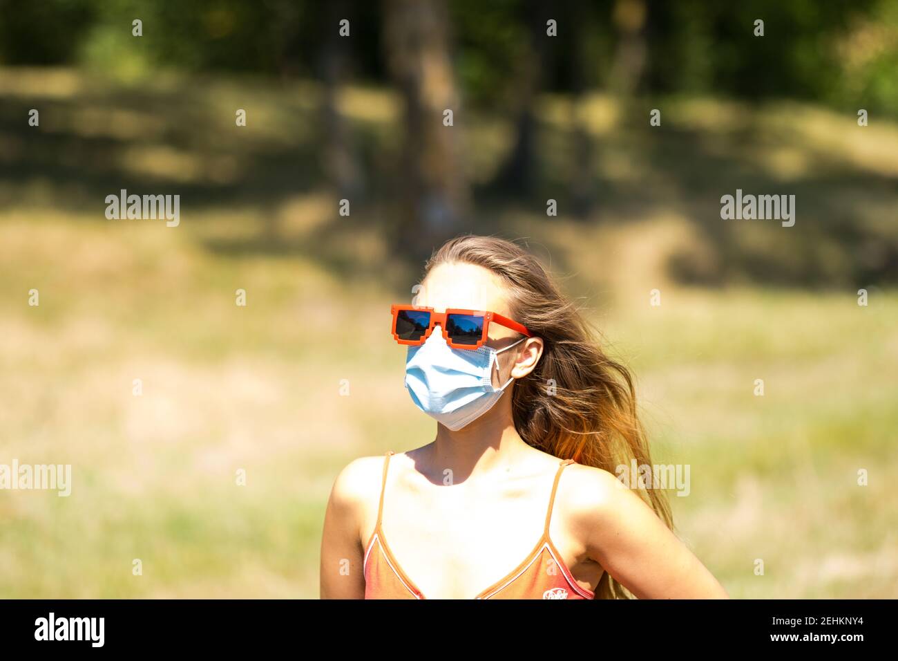 Ragazza con occhiali da sole in pixel rosso che indossa una maschera di precezione in una giornata di sole in tempi pandemici. Foto Stock