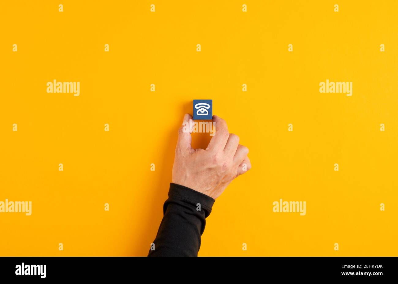 La mano maschile tiene un cubo di legno blu con un'icona del telefono su sfondo giallo. Concetto di contatto, comunicazione o supporto. Foto Stock