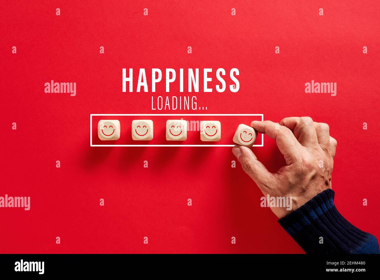Mano maschile mettendo i blocchi di legno con volti sorridenti nella parola felicità barra di caricamento su sfondo rosso. Crescente felicità e positività concetto. Foto Stock