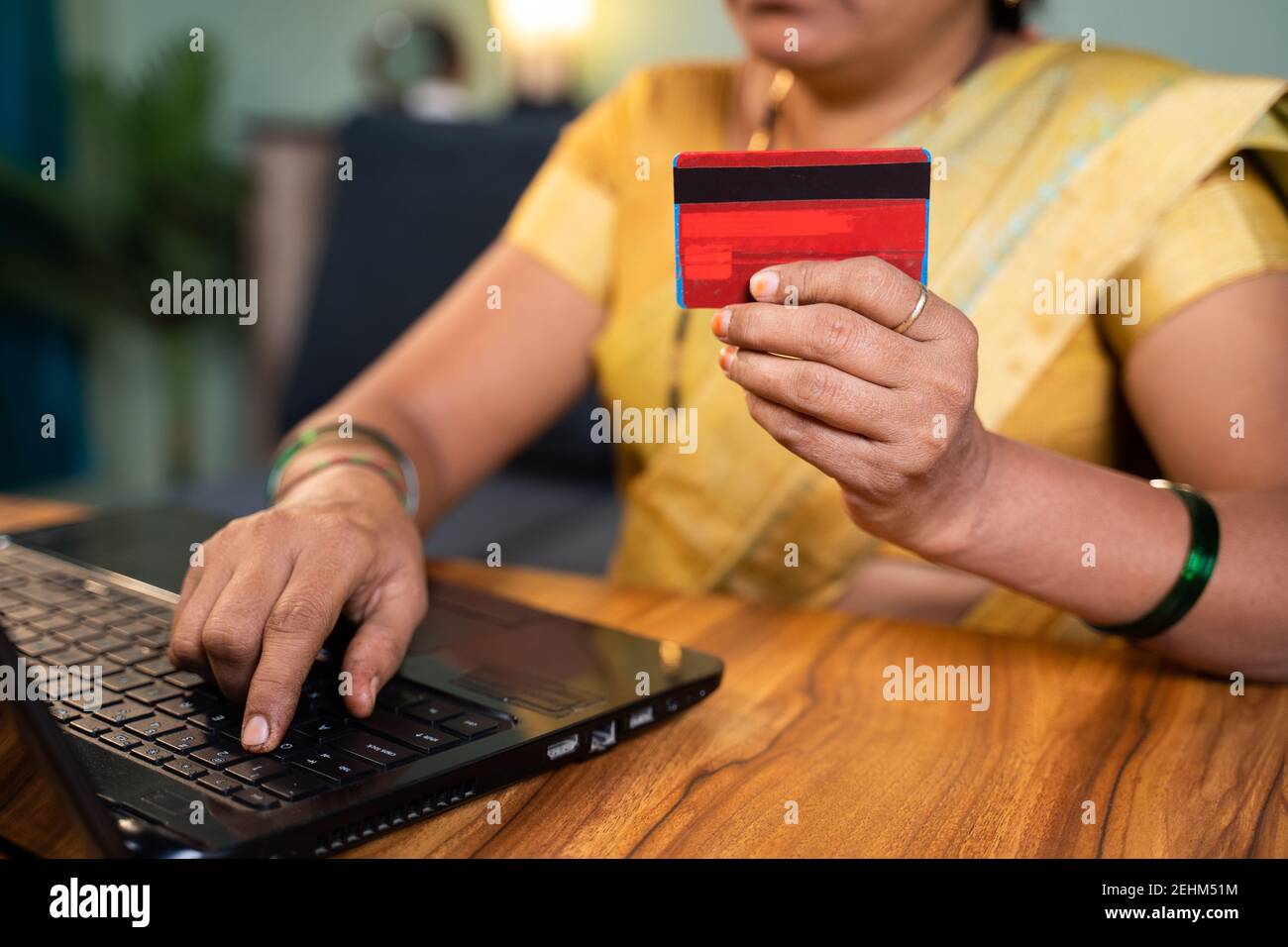 Donna indiana irriconoscibile che agguaglia la carta di credito e che inserisce i dettagli della carta nel laptop per lo shopping online e-commerce o il pagamento della fattura a casa. Foto Stock