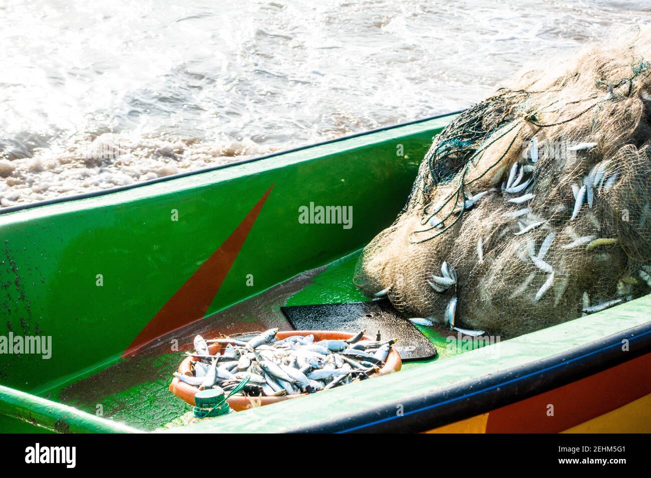 Barca da pesca con rete da pesca piena di pesci e oceano onde sullo sfondo Foto Stock