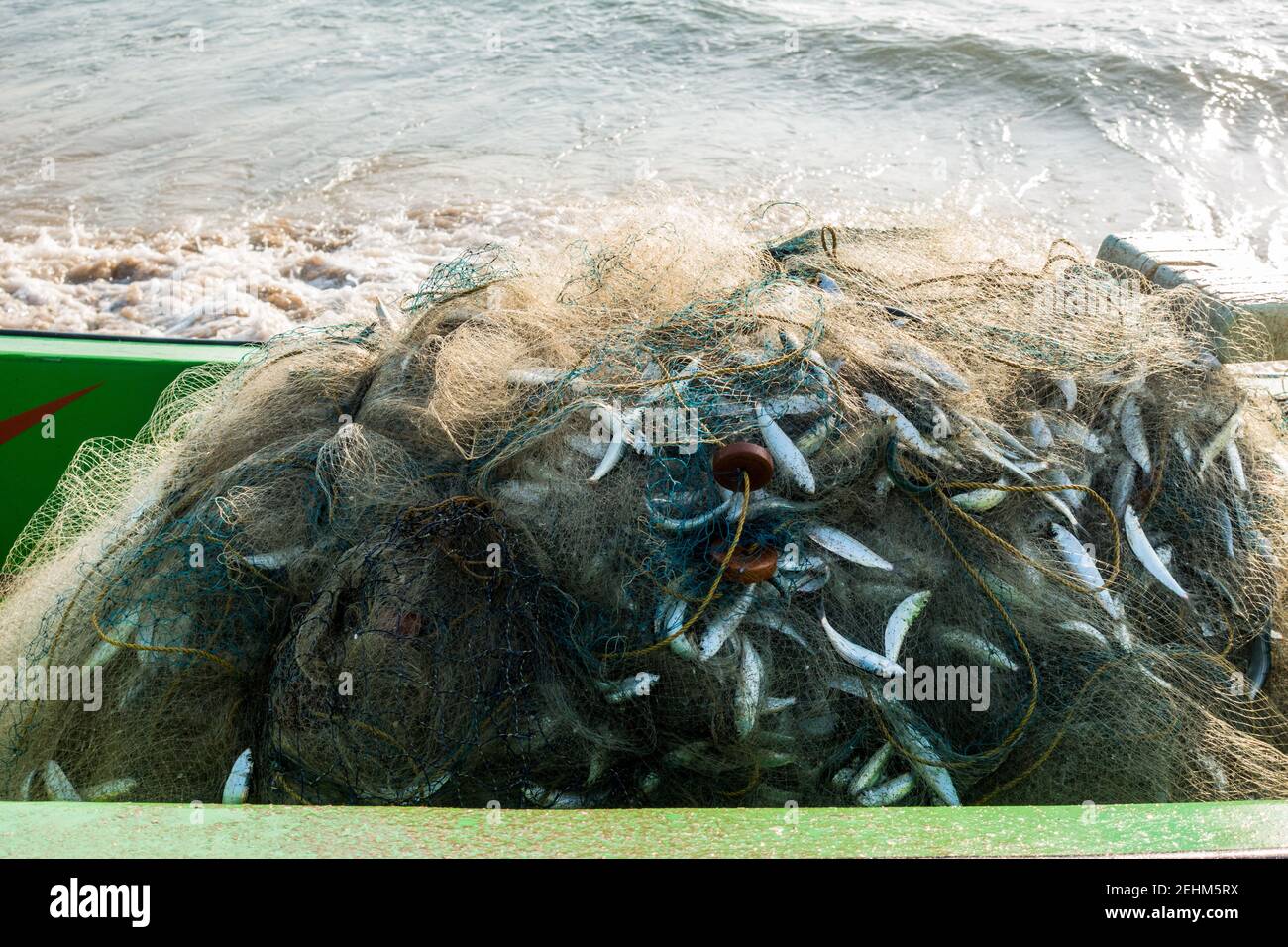 Barca da pesca con rete da pesca piena di pesci e oceano onde sullo sfondo Foto Stock