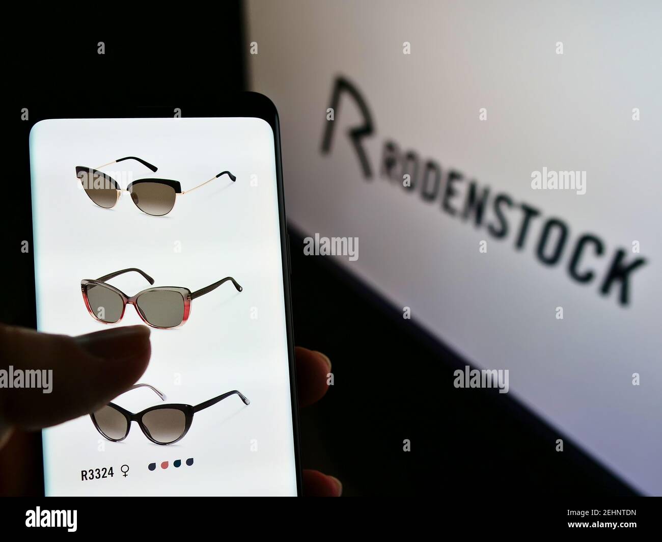 Persona che tiene il cellulare con il sito web aziendale del produttore tedesco di occhiali Rodenstock GmbH sullo schermo di fronte al logo. Mettere a fuoco il display del telefono. Foto Stock