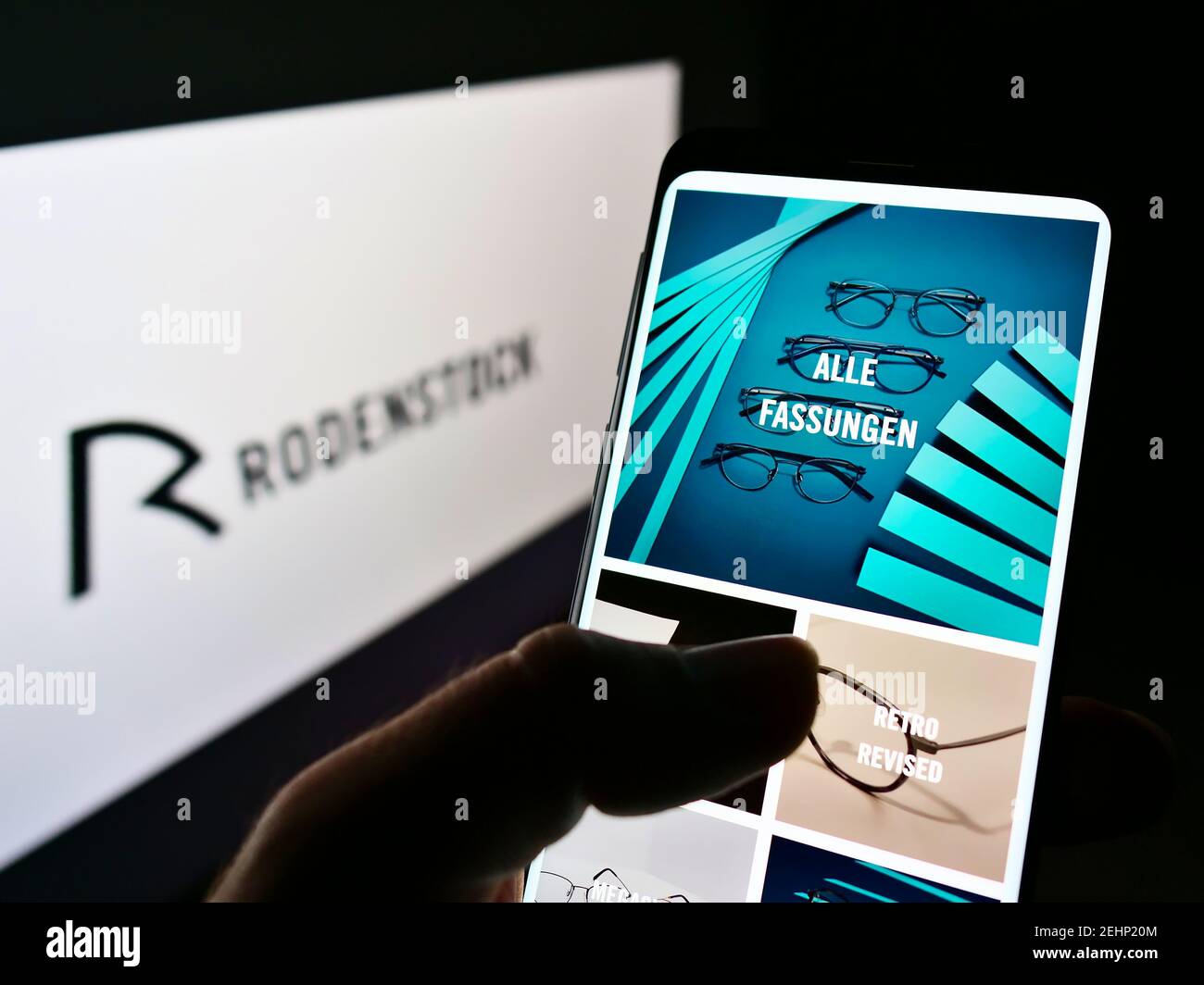 Persona che tiene il cellulare con il sito web del produttore tedesco di occhiali Rodenstock GmbH sullo schermo davanti al logo. Mettere a fuoco la parte superiore centrale del display del telefono. Foto Stock