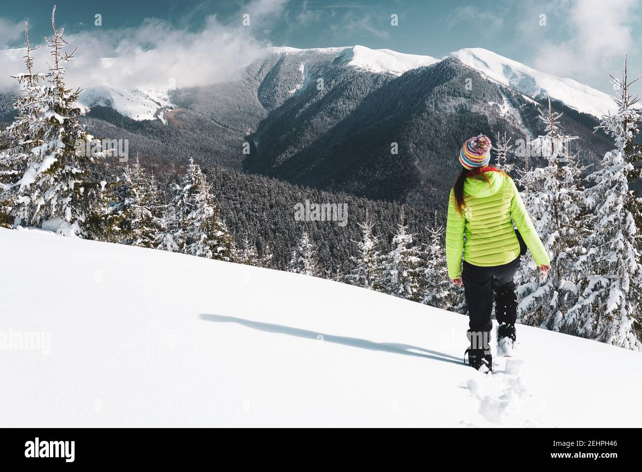 Bellissimo scatto di una donna che cammina su un pendio che domina una foresta durante l'inverno Foto Stock