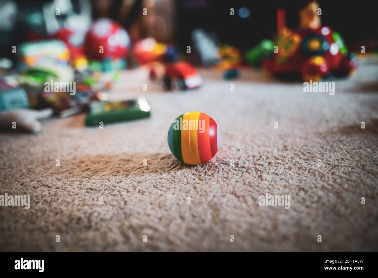 Immagine della profondità di campo bassa (messa a fuoco selettiva) con una sfera di gomma colorata sul pavimento della stanza del bambino, con i giocattoli sullo sfondo. Foto Stock