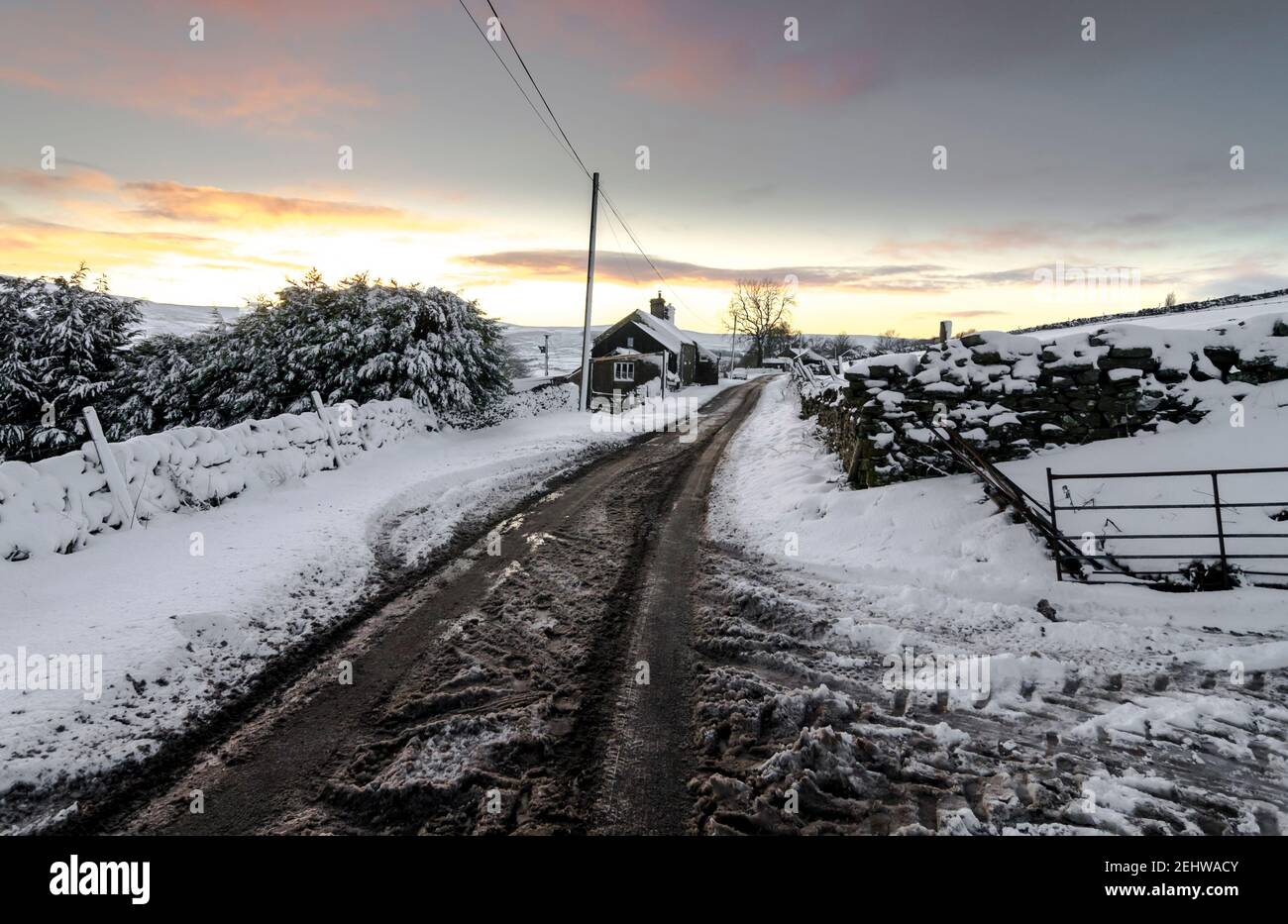 Una corsia di campagna in un paesaggio innevato contro un cielo dorato, nelle prime ore della sera, nel North Pennines, Weardale, County Durham Foto Stock