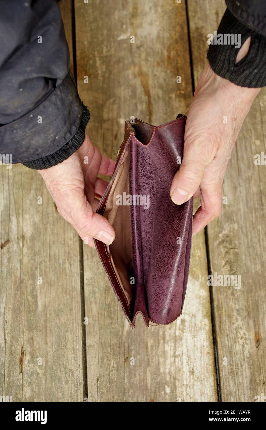 Una donna anziana tiene una borsetta o un portafoglio vuoto su un tavolo di legno d'epoca. Il concetto di povertà in pensione. Povertà estrema globale. Nessun denaro mi aiuta. Foto Stock