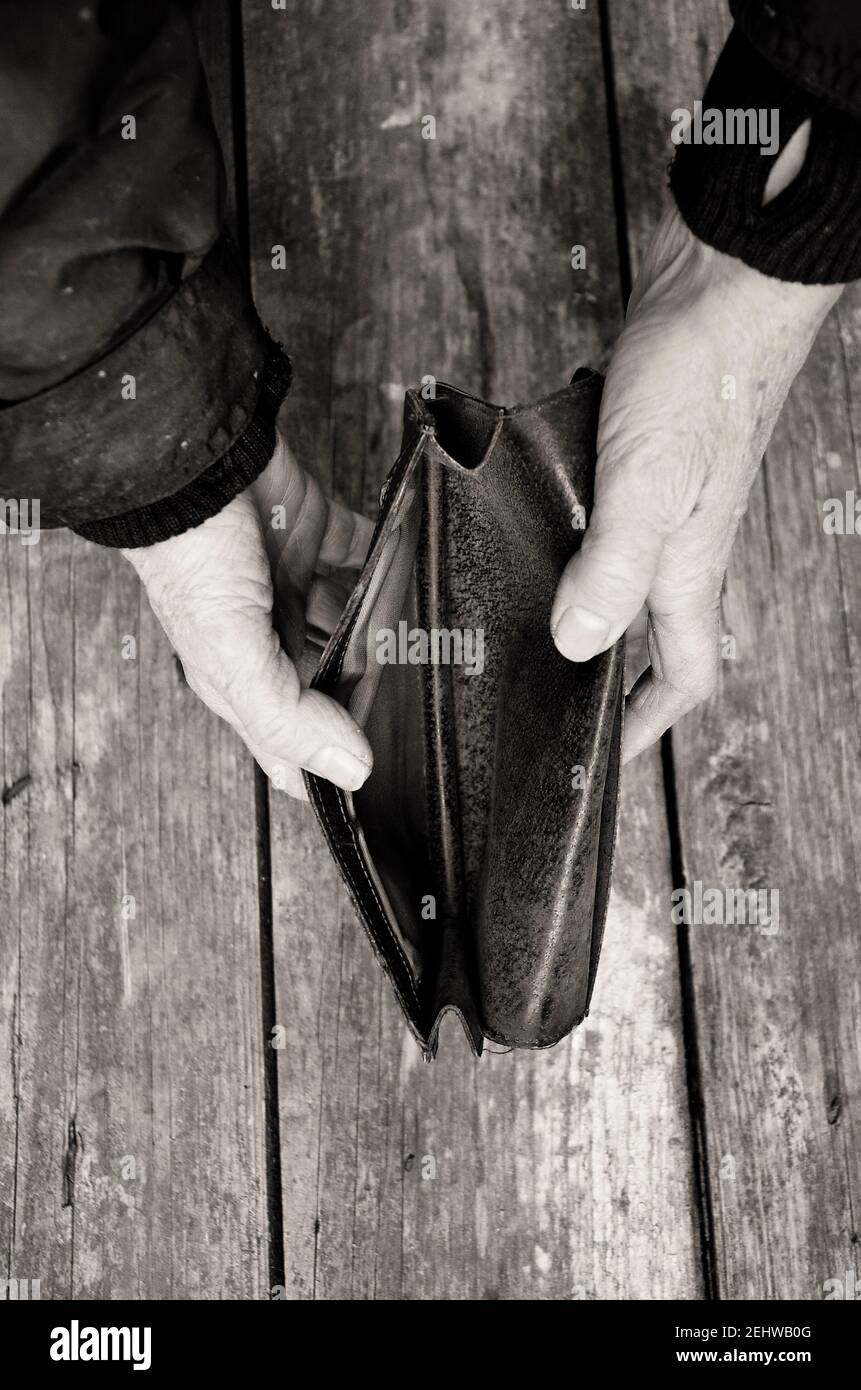 Una donna anziana tiene una borsetta o un portafoglio vuoto su un tavolo di legno d'epoca. Foto in bianco e nero. Il concetto di povertà in pensione. Crisi finanziaria. Foto Stock